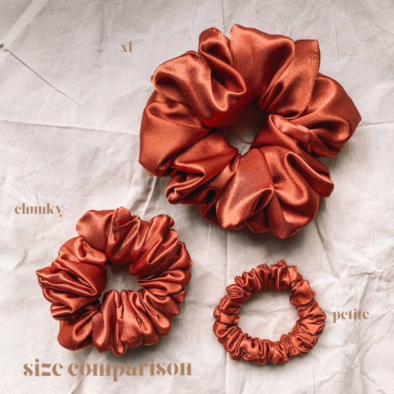 Sunset Glow scrunchie comparison in terracotta, showcasing three sizes: petite, chunky, and XL. The petite scrunchie offers a more delicate, subtle look, the chunky scrunchie adds bold volume, and the XL scrunchie, four times the size of the chunky, provides maximum volume and impact. All scrunchies are made from smooth, luxurious charmeuse silk for a glossy, elegant finish.