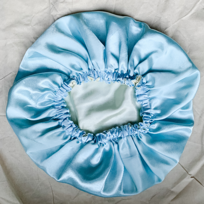 Blueberry Latte reversible silk bonnet in baby blue and ivory . Made from smooth charmeuse silk, this bonnet features a comfortable elastic band for a secure fit, offering a soft, luxurious touch for protecting hair while sleeping or resting