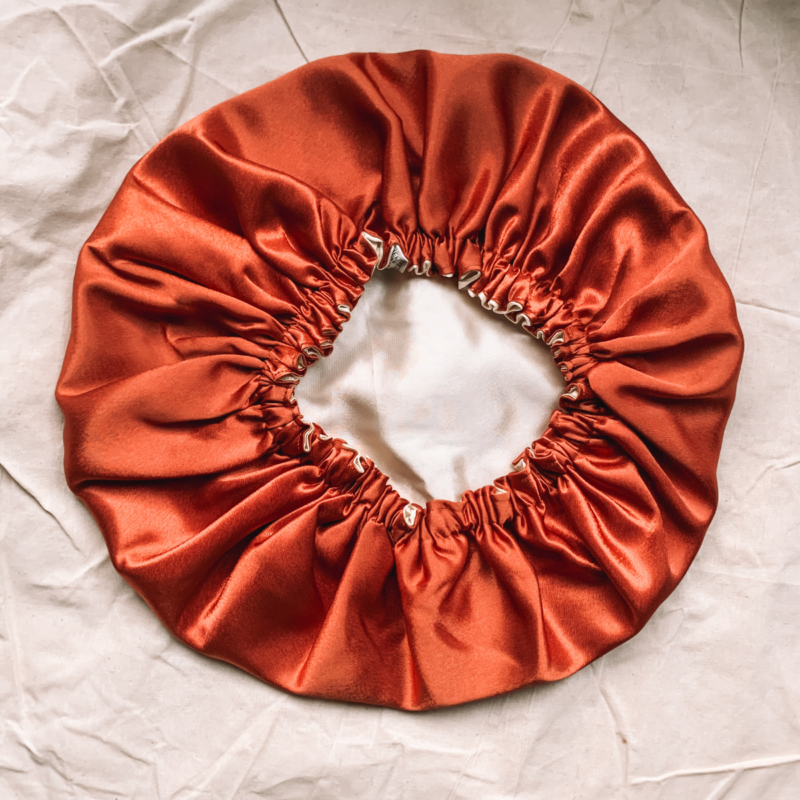 Dusky Sunset reversible silk bonnet in terracotta and cream. Made from smooth charmeuse silk, this bonnet features a comfortable elastic band for a secure fit, offering a soft, luxurious touch for protecting hair while sleeping or resting.