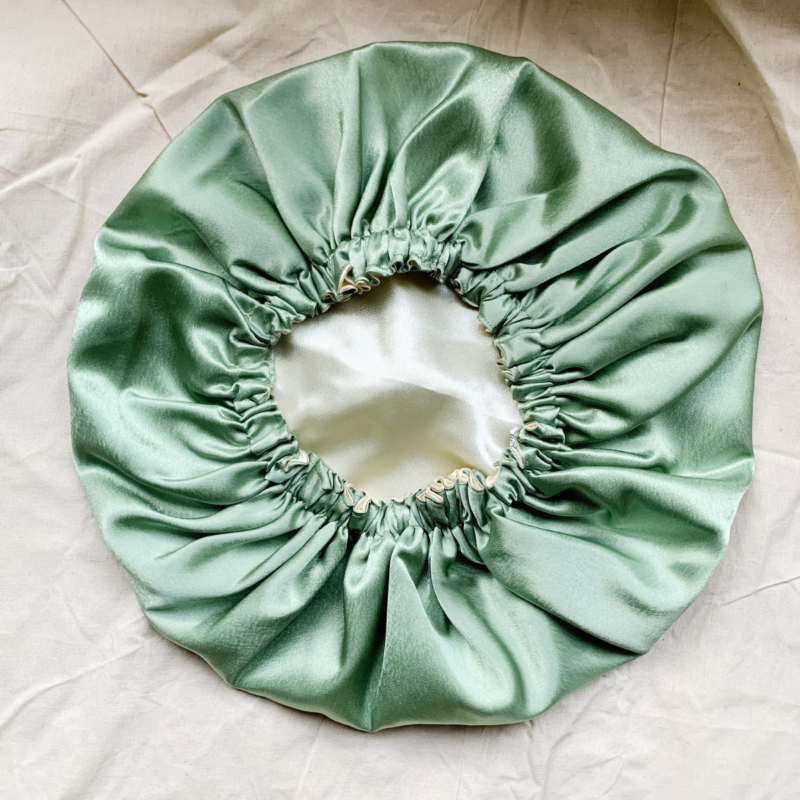 Matcha Latte reversible silk bonnet in sage green and cream . Made from smooth charmeuse silk, this bonnet features a comfortable elastic band for a secure fit, offering a soft, luxurious touch for protecting hair while sleeping or resting.