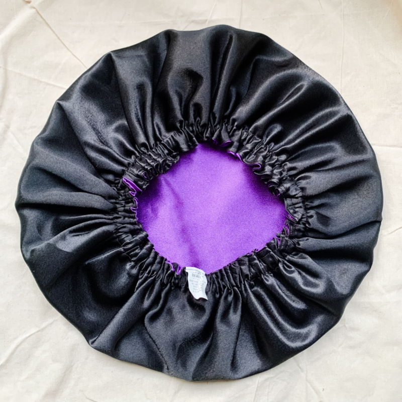 Midnight Amethyst reversible silk bonnet in purple and black. Made from smooth charmeuse silk, this bonnet features a comfortable elastic band for a secure fit, offering a soft, luxurious touch for protecting hair while sleeping or resting.