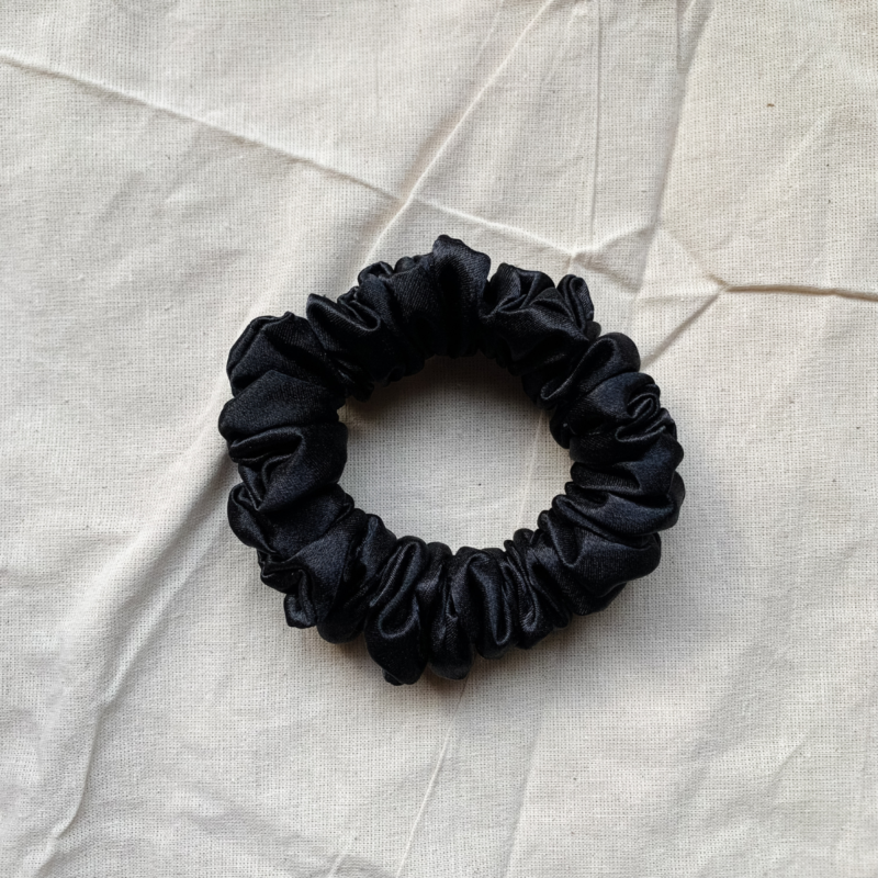 Noir black petit scrunchie made from luxe charmeuse satin. Oversized design, approximately twice the size of a standard scrunchie, with a smooth, glossy finish that adds a touch of elegance to any hairstyle.