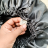 Noir reversible silk bonnet in black. Made from smooth charmeuse silk, this bonnet features a comfortable elastic band for a secure fit, offering a soft, luxurious touch for protecting hair while sleeping or resting.