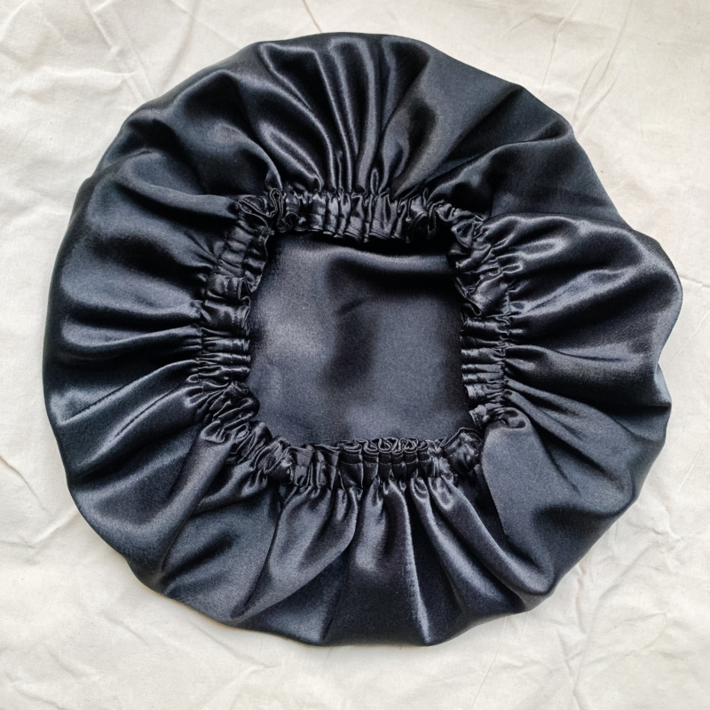 Noir reversible silk bonnet in black. Made from smooth charmeuse silk, this bonnet features a comfortable elastic band for a secure fit, offering a soft, luxurious touch for protecting hair while sleeping or resting.