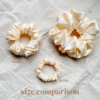 Oatmilk scrunchie comparison in soft cream, showcasing three sizes: petite, chunky, and XL. The petite scrunchie offers a more delicate, subtle look, the chunky scrunchie adds bold volume, and the XL scrunchie, four times the size of the chunky, provides maximum volume and impact. All scrunchies are made from smooth, luxurious charmeuse silk for a glossy, elegant finish.