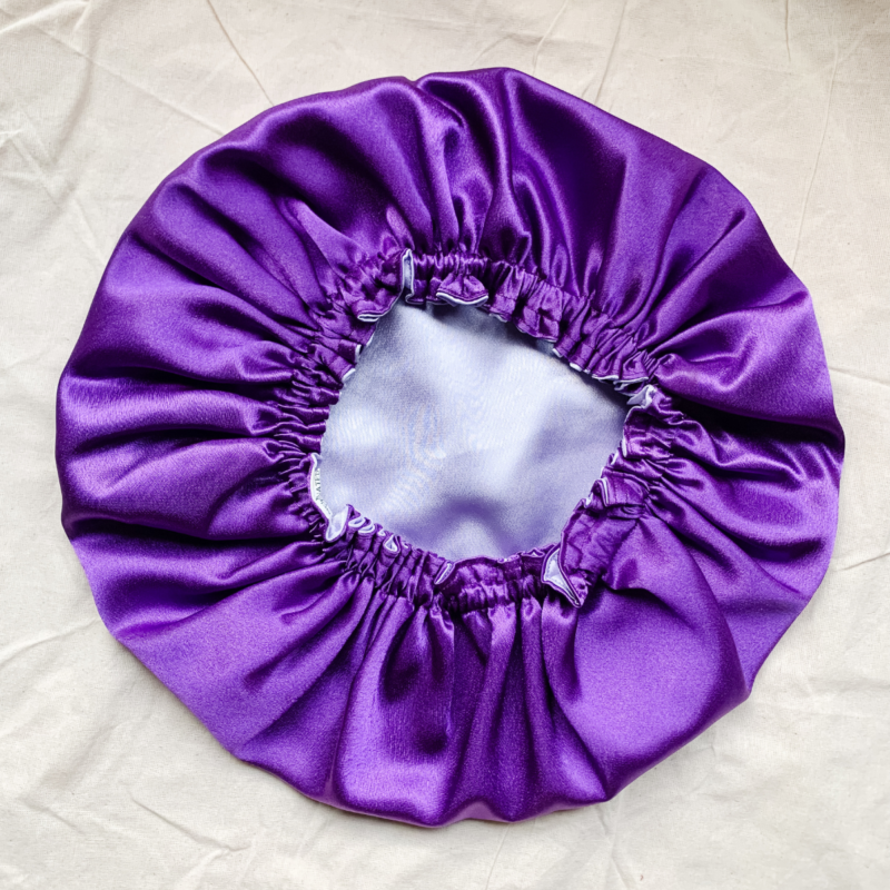 Purple Haze reversible silk bonnet in purple and lavender. Made from smooth charmeuse silk, this bonnet features a comfortable elastic band for a secure fit, offering a soft, luxurious touch for protecting hair while sleeping or resting.