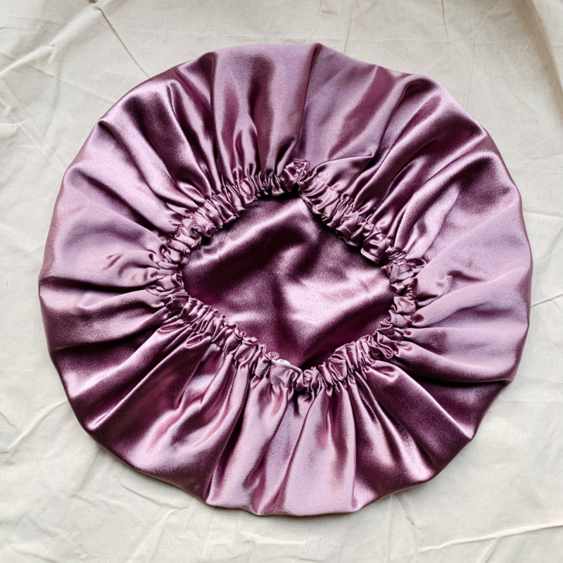 Rosé Glow reversible silk bonnet in metallic mauve. Made from smooth charmeuse silk, this bonnet features a comfortable elastic band for a secure fit, offering a soft, luxurious touch for protecting hair while sleeping or resting.