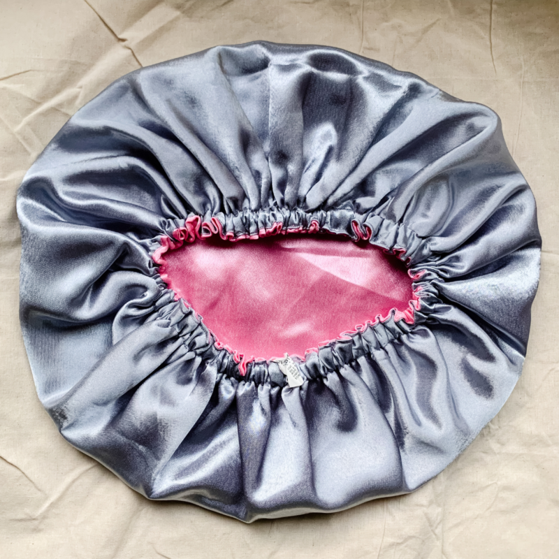 Silver Rose reversible silk bonnet in silver and light pink. Made from smooth charmeuse silk, this bonnet features a comfortable elastic band for a secure fit, offering a soft, luxurious touch for protecting hair while sleeping or resting.